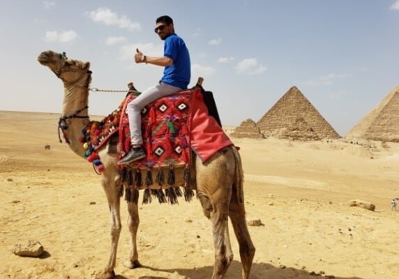 A pearson riding a camel with Giza Pyramids in the background