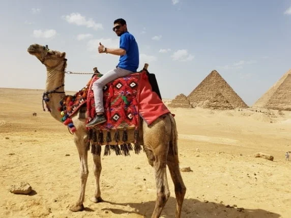 A pearson riding a camel with Giza Pyramids in the background