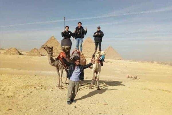 Three people standing on top of camels, with a tour guide in at Giza Pyramids in Egypt