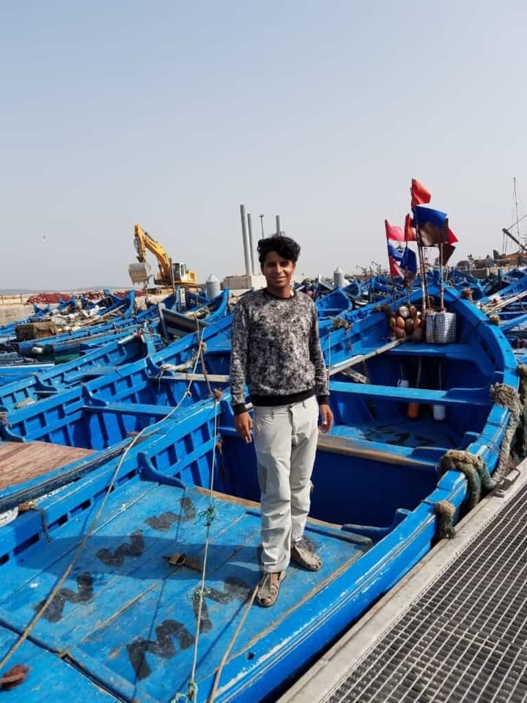 A person posing for a photo standing on a blue boat inEssaouira Morocco