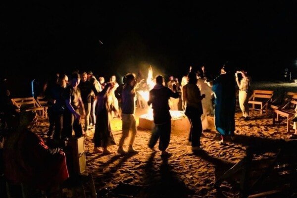 Group of people dancing around a Sahara Desert Camp fire pit at night