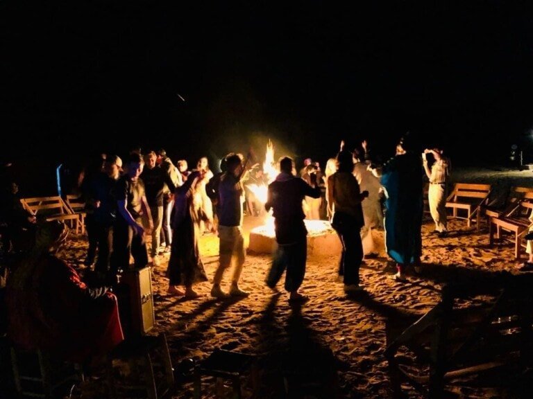 Group of people dancing around a Sahara Desert Camp fire pit at night