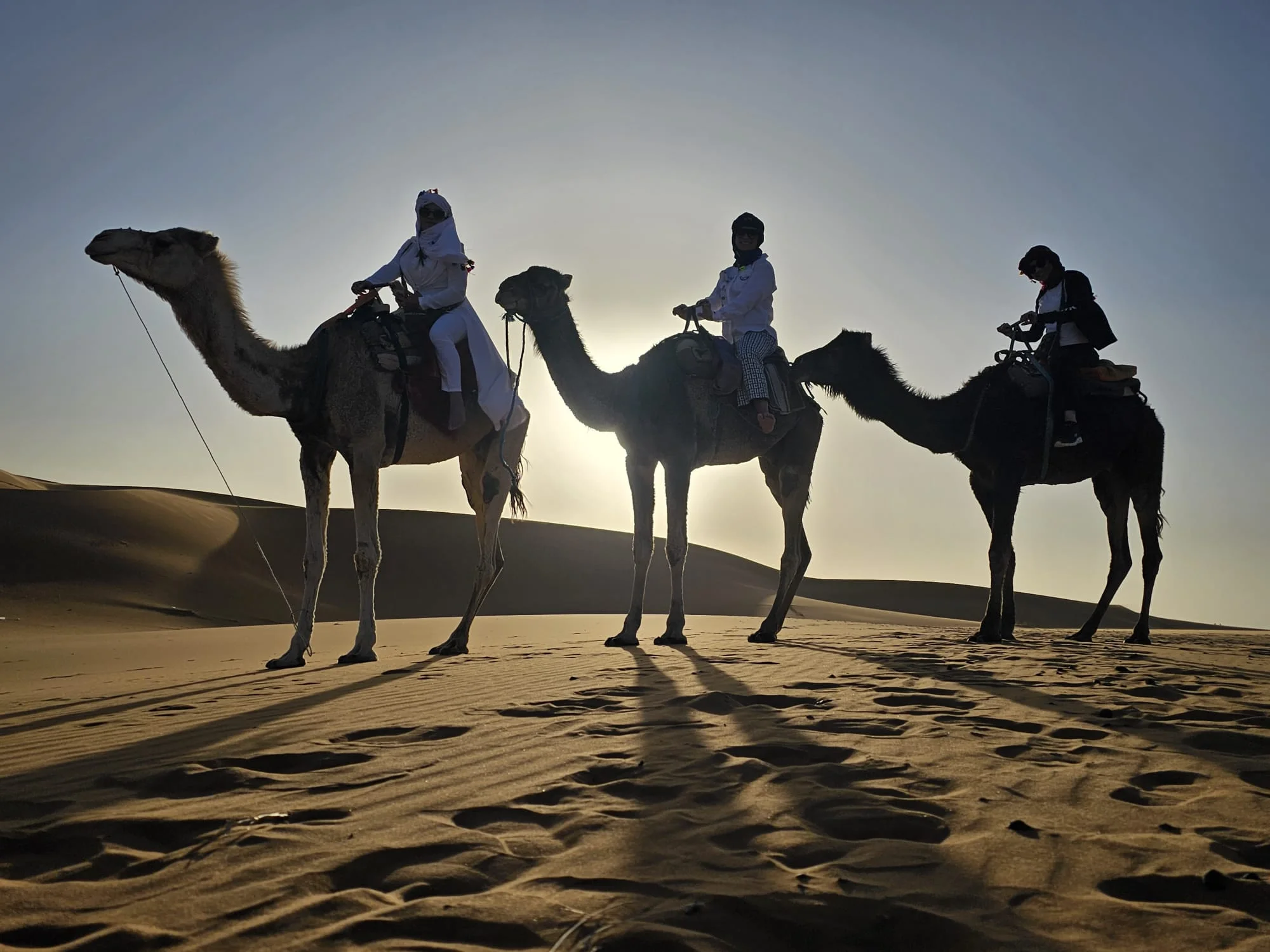 Couple with a local guide riding camels at the Sahara Desert