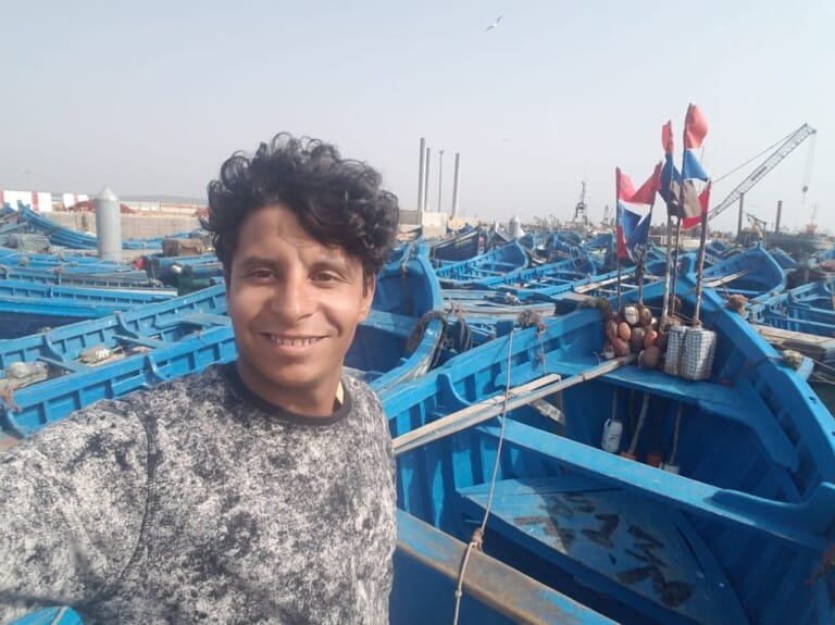A person posing with iconic blue boats in background at Essaouira